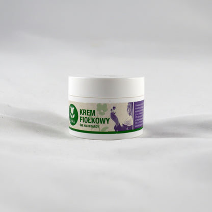 A white plastic jar of Jura violet st Hildegard cream with a white, green, and purple label, set against a plain light gray background. 